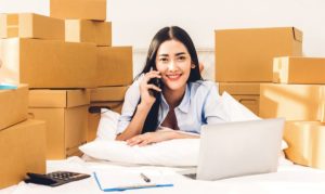 Una emprendedora gestionando su negocio desde su laptop, y en el fondo una pila de paquetes de envíos pertenecientes a su negocio; esto en referencia a la nueva alianza de Bling con Amazon para beneficiar a Pymes en México.