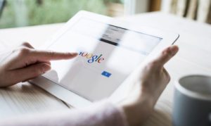 Una usuaria en México haciendo búsquedas online en Google desde su tablet. La vemos sosteniendo el dispositivo, y a un costado una taza de café.