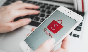 mano que sostiene un teléfono móvil que muestra la pantalla principal de la tienda online de Shopee, representado su historia en México