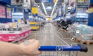 carrito de supermercado físico con las manos de un consumidor, que muestra sobrepuesto una pantalla digital con varios canales, representando cómo la inteligencia artificial y la omnicanalidad ayudan al retail.