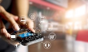 Plano detalle de una mano sosteniendo un celular, del que se desprenden íconos digitales referentes al comercio omnicanal eN México (carrito de compras, laptop, celular, internet, audífonos, etc.)