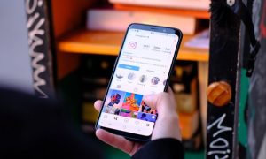 Fotografía de la mano de una persona sosteniendo un teléfono móvil en el que se muestra un perfil de Instagram.