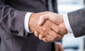 Plano detalle de dos hombres en traje estrechándose la mano en muestra de apoyo y colaboración; esto en referencia a la declaración de la Concanaco para colaborar con plataformas de eCommerce en busca de generar sana competencia.
