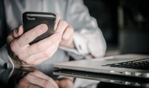 Usuario haciendo transferencia a través de Dimo STP. Lo vemos sosteniendo su celular, y a un costado tiene una laptop.