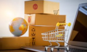 Una figura de un mundo sobre unas cajas de pedidos de eCommerce, y a un costado un carrito de compras encima de una laptop. Esto en referencia al crecimiento del cross-border en plataformas como eBay.