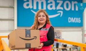 Una colaboradora de Amazon México sosteniendo un paquete y vistiendo su uniforme, ya que forma parte de la nueva plantilla temporal de empleados del marketplace en México.