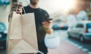 Repartidor de Glup entregando en una bolsa una orden de delivery. Lo vemos sosteniendo una bolsa, su celular y su casco.