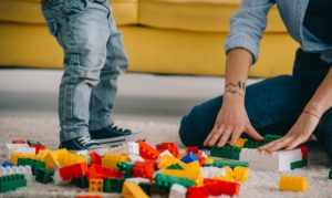 Plano medio de una mamá jugando con su hijo Lego, con bloques y piezas tiradas sobre el suelo; esto en referencia a la venta online de estos productos en México.