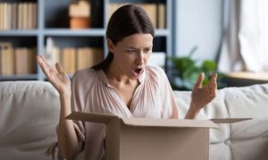 Plano medio de una mujer abriendo un pedido online y con cara de asombro y enojo, lo que provocará una intención de devolución; esto en referencia a la importancia de tercerizar la logística inversa en eCommerce.