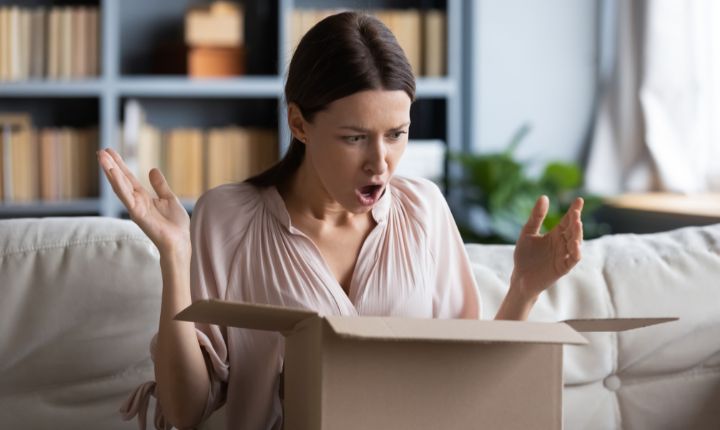 Plano medio de una mujer abriendo un pedido online y con cara de asombro y enojo, lo que provocará una intención de devolución; esto en referencia a la importancia de tercerizar la logística inversa en eCommerce.