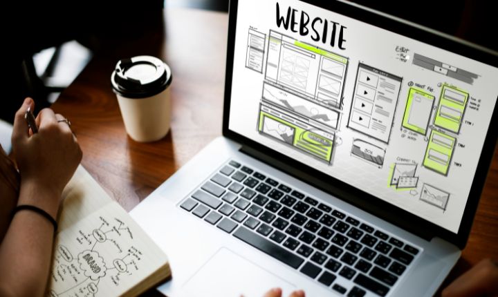 Un usuario dándole mantenimiento a su sitio web desde su laptop, tomando nota en una libreta.