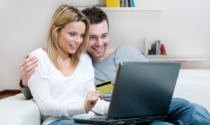Una pareja navegando desde su laptop, conociendo las ofertas de las marcas antes de El Buen Fin. Sostienen una tarjeta de crédito y una laptop en su regazo.