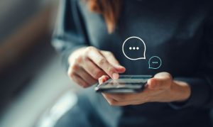 Chica con su celular en mano, aprovechando las estrategias de marketing conversacional en México para comprar productos online. Del celular sobre salen unos íconos de mensajes de texto.
