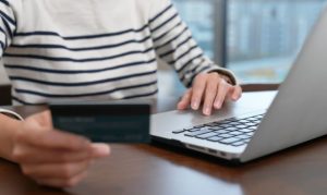 Plano medio corto de una mujer en México haciendo compras online desde su laptop mientras sostiene una tarjeta de crédito en su mano.