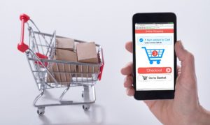 Una mano sosteniendo un celular que despliega el checkout de una compra, y de fondo un carrito con pedidos; esto en referencia a la incursión de las mipymes mexicanas en eCommerce.