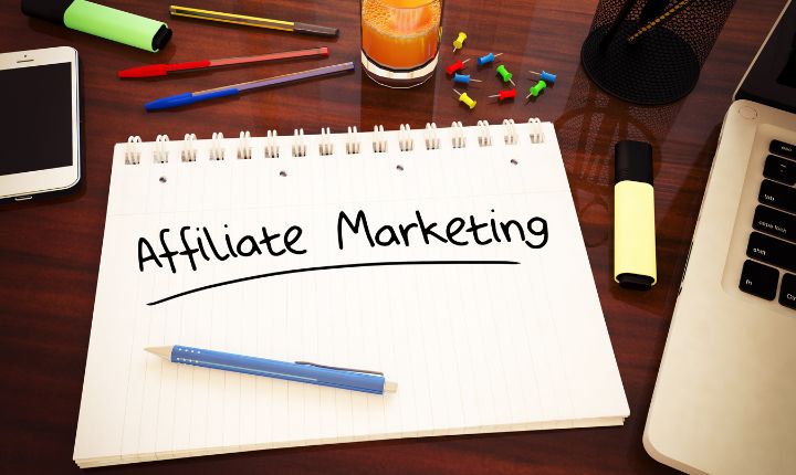 Toma picada de una libreta en la que se lee "affiliate marketing", acompañada de una laptop y plumones.