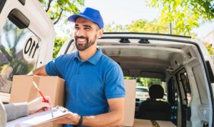 Repartidor de Moova entregando un paquete. Vemos su camioneta de delivery, y el repartidor ocupa una playera y gorra azul.