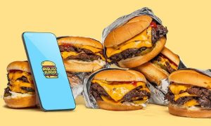 Conjunto de hamburguesas de MrBeast Burger, con fondo amarillo y un celular en el que apreciamos la identidad gráfica de la marca.