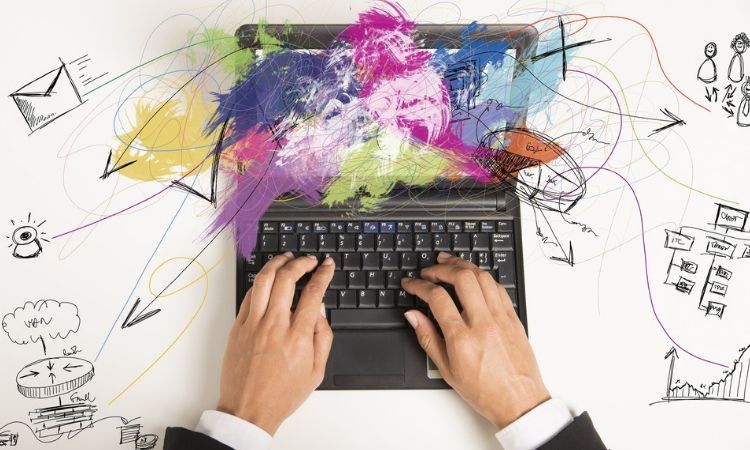 manos de una persona formal vestida con traje tecleando en una laptop de la que salen diferentes colores mostrando Qué es e-marketing y qué implica
