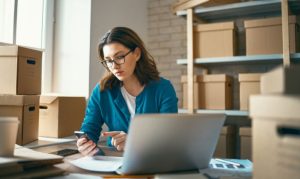 Una emprendedora vendiendo desde Rocketfy. La vemos utilizando su laptop mientras está sentada en un almacén, donde guarda sus pedidos online.