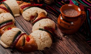 Toma picada de una rosca de reyes magos, a un costado encontramos una taza de chocolate caliente. Esto en referencia a los pedidos online de rosca de reyes en México.