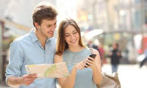 Una pareja mirando destinos turísticos en su celular, mientras uno de ellos sostiene el mapa de una ciudad; esto en referencia a las tendencias de viaje 2024 desveladas por Airbnb.