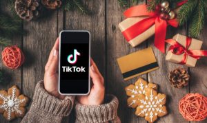 Toma cenital de una usuaria haciendo compras navideñas en TikTok desde su celular. A su alrededor encontramos decoraciones navideñas, como regalos, galletas, piñas de árbol y demás.