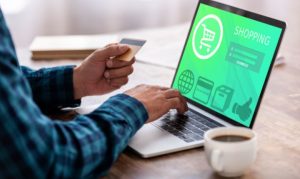 Un hombre sentado y haciendo compras online desde su laptop mientras sostiene una tarjeta de crédito; esto en referencia al uso de estos medios de pago (y débito) en eCommerce.