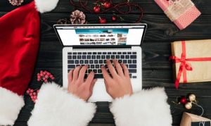 Toma cenital de un internauta haciendo compras online durante el Guadalupe Reyes, periodo en el cual las marcas mexicanas aumentan sus ventas. Vemos al comprador vistiendo una gabardina parecida a la de Santa Claus y en la mesa artículos relacionados a Navidad.