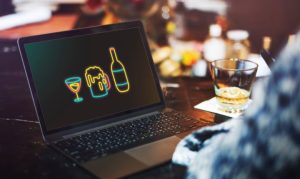 Plano escorzo de un hombre con camisa a cuadros sentado frente a una laptop con íconos de vinos y licores, en referencia al impulso que toman estos productos en eCommerce.